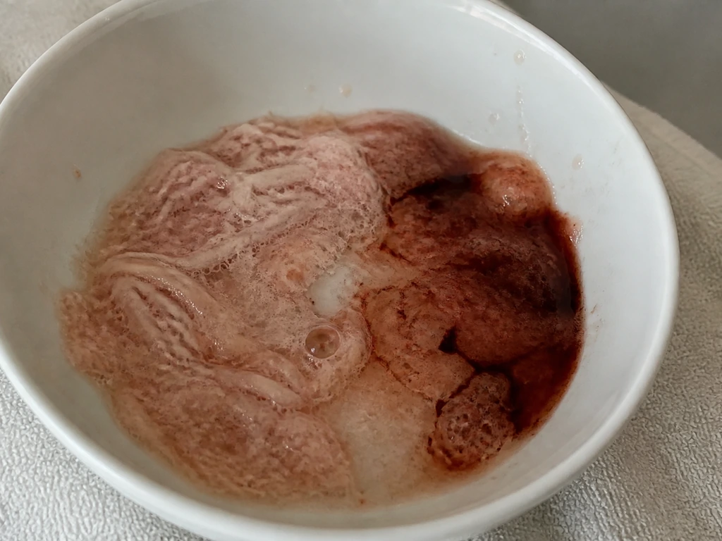 Close-up van lichtroze schuim en roodbruine sporen in braaksel, ter vergelijking van kleurverschillen.